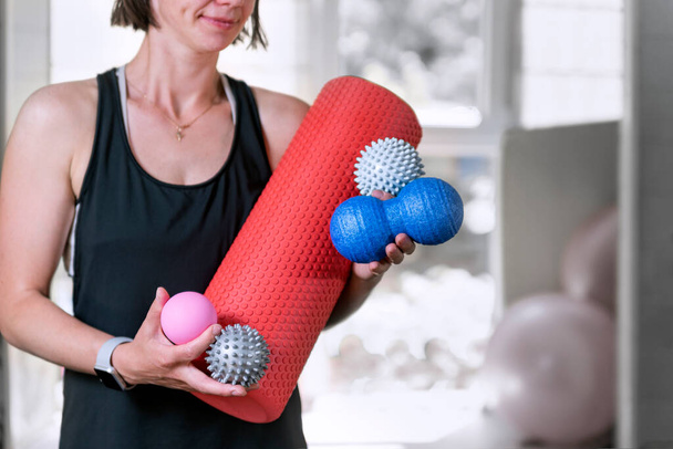 Young sportswoman in the gym stands with different types of myofascial rolls. Equipment for MFR. Roller for physiotherapy - Foto, immagini
