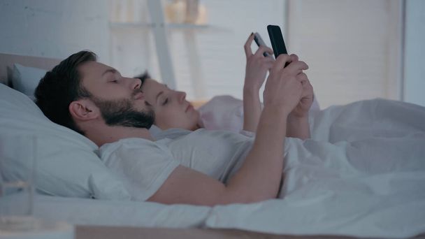 Young couple using smartphones on bed at home  - Φωτογραφία, εικόνα