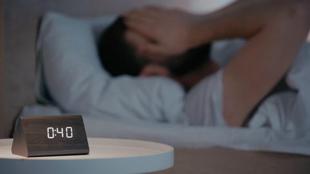 Clock on bedside table near blurred man on bed at night  - Foto, Imagem