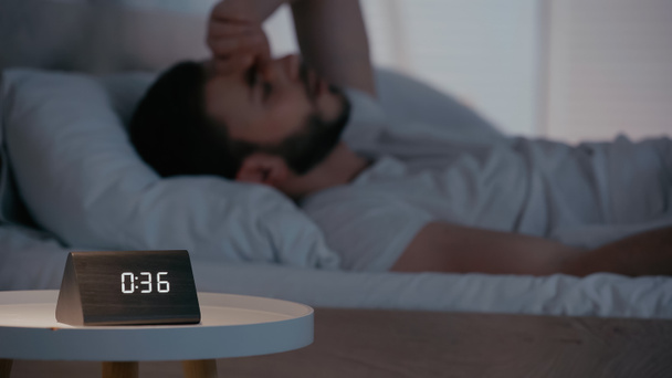 Clock on bedside table near blurred man in bedroom at night  - Фото, изображение