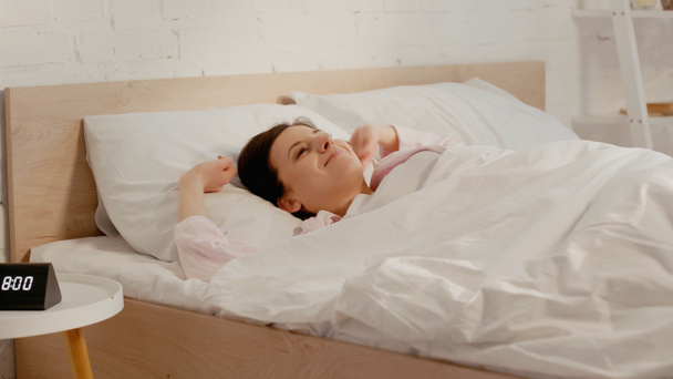 Cheerful woman lying on bed near clock on bedside table  - Фото, зображення