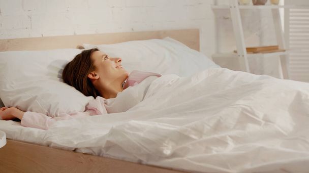 Positive brunette woman lying on bed at home  - Valokuva, kuva
