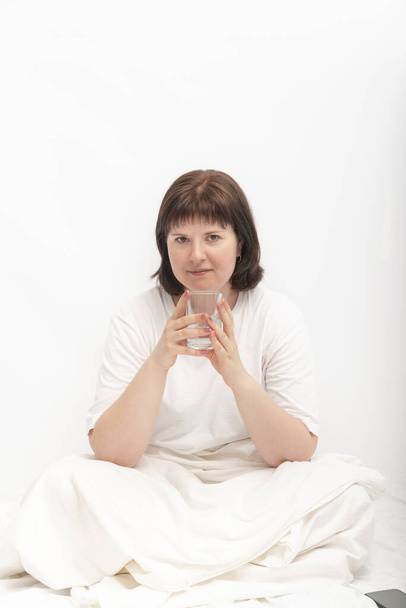 Egy fiatal kaukázusi nő portréja az ágyban egy pohár vízzel. Az ivóvíz szokása reggel - Fotó, kép