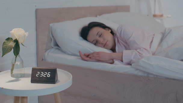 Clock and plant near blurred woman sleeping on bed at night  - Valokuva, kuva