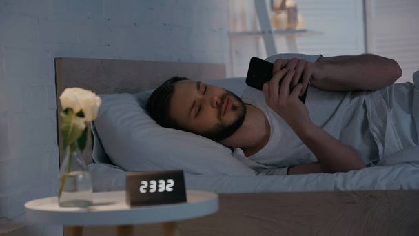 Fiatal férfi használ okostelefon az ágyban éjszaka  - Fotó, kép