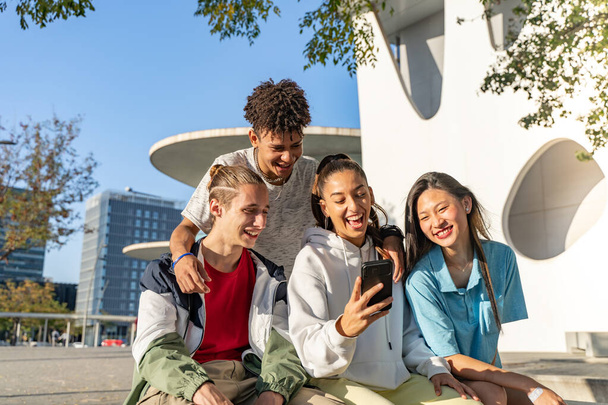 Group of happy teenage friends looking the phone and laughing in the city street. - Photo, Image