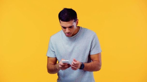 young man in t-shirt using smartphone isolated on yellow  - Foto, Imagen