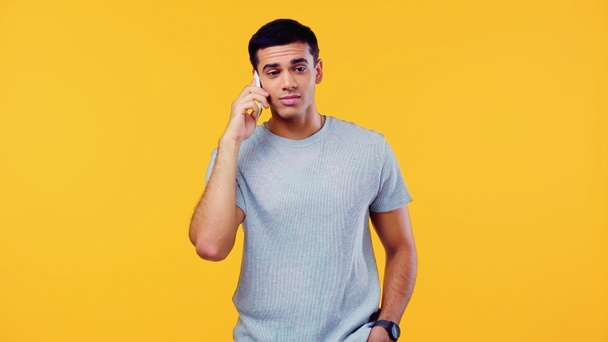 confused young man in t-shirt talking on mobile phone isolated on yellow  - Foto, Imagen