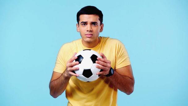 zdůraznil mladý muž ve žlutém tričku drží fotbal izolovaný na modré - Fotografie, Obrázek