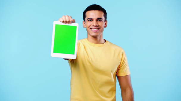 gelukkig jongeman in geel t-shirt met digitale tablet met groen scherm geïsoleerd op blauw - Foto, afbeelding