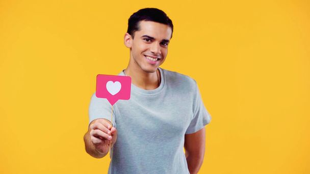 joyeux jeune homme en t-shirt tenant coeur sur bâton isolé sur jaune - Photo, image