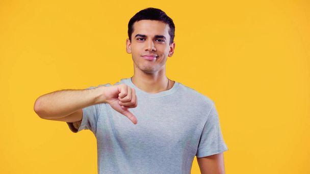 dissatisfied young man in t-shirt showing dislike isolated on yellow - Photo, Image