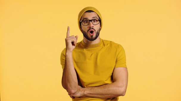 surprised young man in beanie hat showing idea sign isolated on yellow  - Foto, Bild