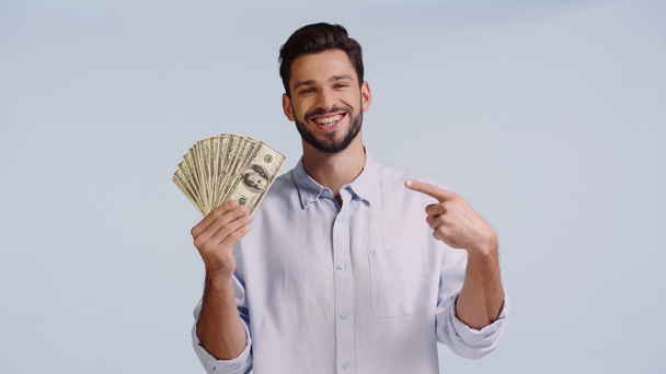 vrolijk man in shirt kijken naar camera terwijl wijzend op dollars geïsoleerd op blauw  - Foto, afbeelding