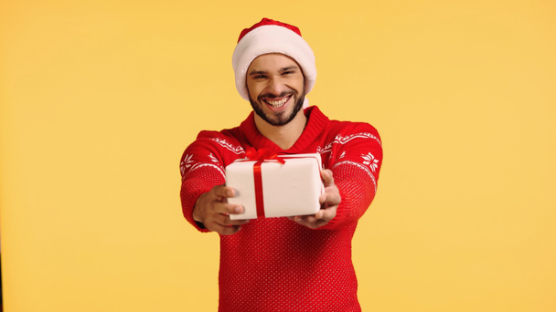 smiling man in santa hat holding gift box isolated on yellow - Φωτογραφία, εικόνα