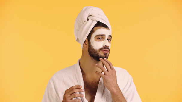 man met baard met klei masker op gezicht geïsoleerd op geel - Foto, afbeelding