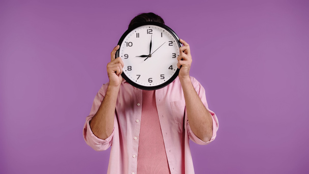 young man obscuring face with clock isolated on purple - Foto, immagini