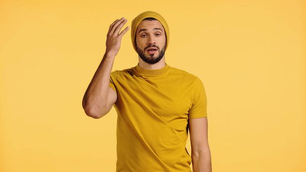 nespokojený mladý muž v čepici gestikulující izolovaně na žluté  - Fotografie, Obrázek