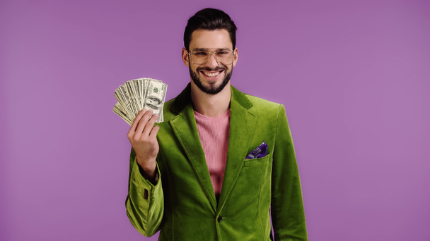 onnellinen mies vihreä takki ja lasit tilalla dollareita eristetty violetti - Valokuva, kuva