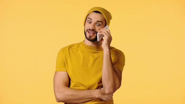 ビーニーの帽子をかぶった笑顔の男が黄色で隔絶されたスマートフォンで - 写真・画像