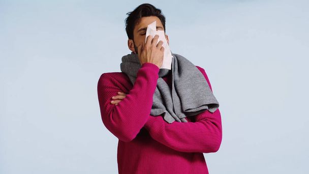 sick man in pink sweater and scarf sneezing in napkin isolated on blue  - Photo, Image