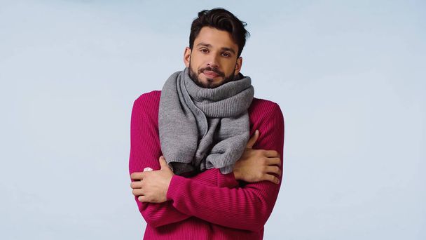 ピンク色のセーターとスカーフを着た病気の男が腕を組んで立っている間に冷たい青で隔離された感じ  - 写真・画像