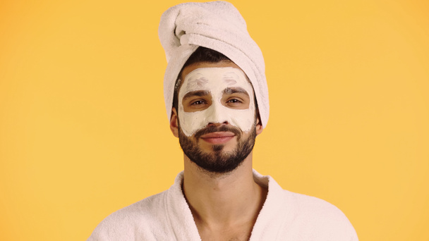 pleased man with clay mask on face looking at camera isolated on yellow - Foto, Bild