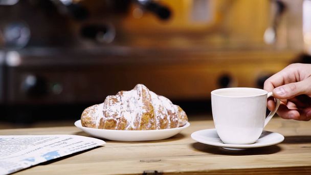 vista recortada del hombre tomando taza cerca de croissant en la cafetería  - Foto, imagen