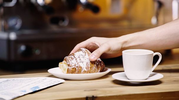 обрезанный вид человека, принимающего круассан возле чашки в кафе  - Фото, изображение