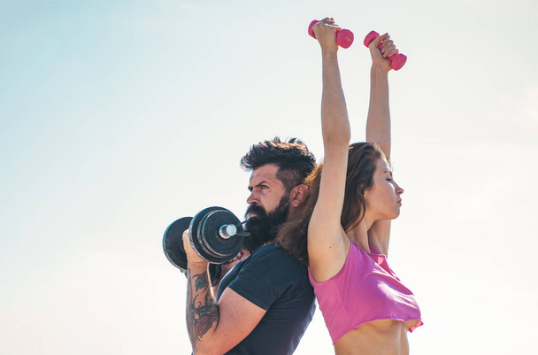 Fit sexy couple on sky background with dumbbells. Fitness concept. Sports couple training with dumbbell. Healthy coupl life style. Sporty woman in sexy pink sportswear. - Foto, immagini