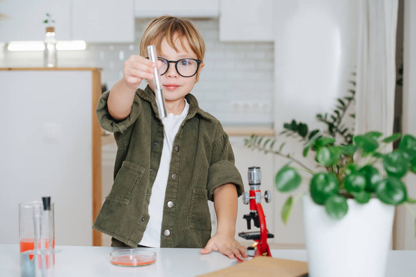 Confident little boy doing science project, showing a flask with clear liquid - Fotó, kép