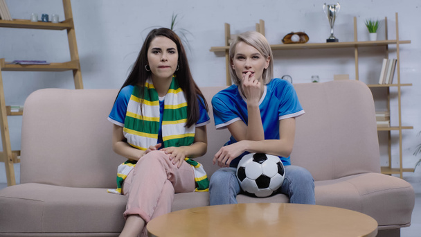 tense women with striped scarf and soccer ball watching football match on tv at home - Foto, Imagem