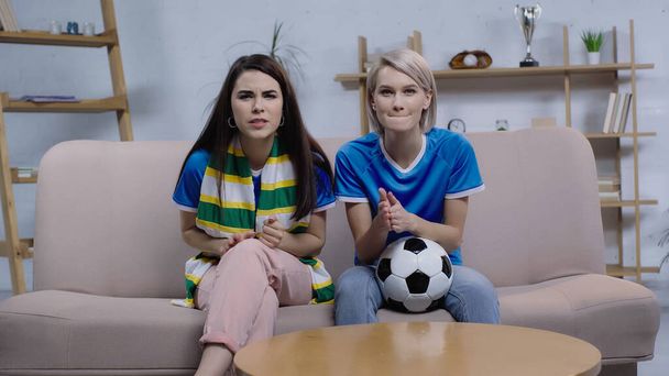 worried football fans watching championship near soccer ball on sofa at home - Foto, Imagem