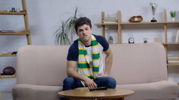 Frustrierter junger Sportfan sieht Spiel im Fernsehen, während er zu Hause auf dem Sofa sitzt - Foto, Bild