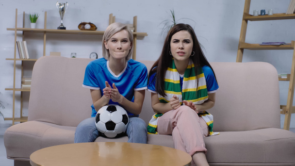 worried sport fans with soccer ball and striped scarf watching football match on home tv - Photo, Image