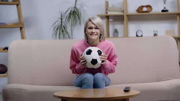 worried sport fan woman holding soccer ball while watching game on tv at home - Foto, afbeelding