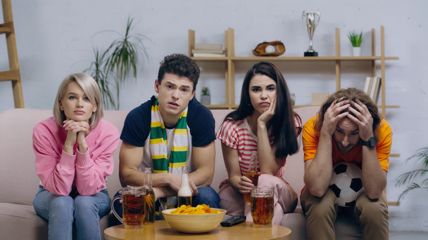 unhappy football fans watching match on tv while sitting on couch near beer and chips - Photo, Image