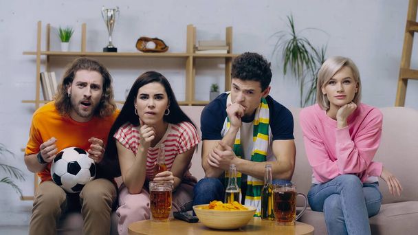 amigos preocupados haciendo gestos mientras ve el partido de fútbol en la televisión cerca de cerveza y patatas fritas - Foto, Imagen