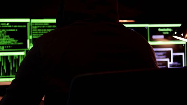 El ciberhacker con capucha sentado examina los datos. Introduzca sistemas protegidos para robar dinero e información. Concepto de ciberterrorismo. - Foto, imagen