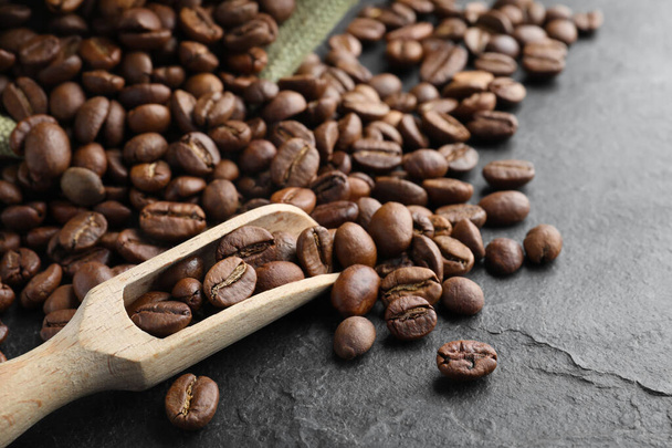 Wooden scoop with roasted coffee beans on black table, closeup - Photo, Image