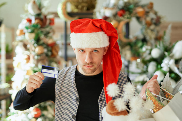Vážný muž v klobouku Santa drží nákupní tašky a kreditní karty - Fotografie, Obrázek