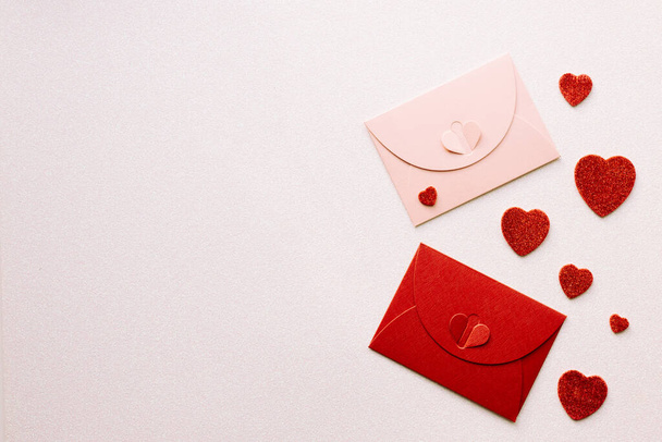 dekorativní červené a růžové obálky s uzávěrem symbolizující lásku na stříbřitě lesklém pozadí, Rozptýlené červené třpytky srdce, Místo pro přání nebo vyznání lásky  - Fotografie, Obrázek