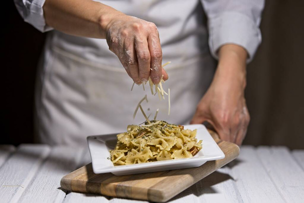 Studio photo of sprinkling  parmesan cheese onto a plate of bowtie pasta.  - Photo, Image