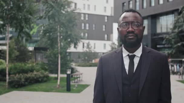 Retrato de seguimiento del hombre de negocios afroamericano con traje y gafas posando para la cámara afuera - Metraje, vídeo