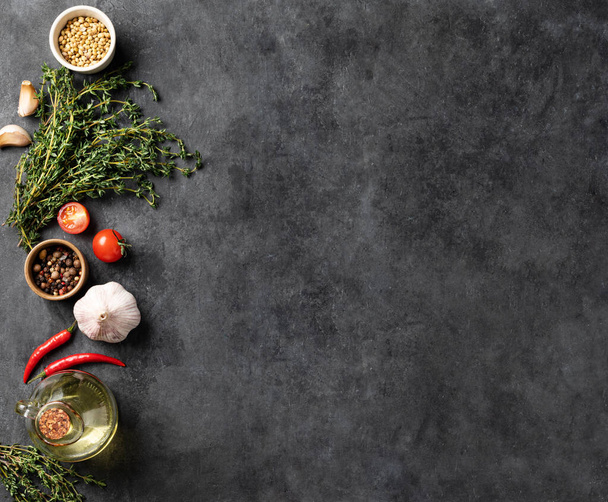 Seasonings, spices and fresh herbs thyme, coriander, garlic, pepper,  tomatoes chili pepper on a dark gray background. The concept of delicious and healthy cooking. Top view and copy space. - Фото, изображение