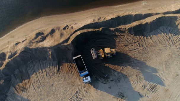 Zandmijnbouw, zandmijn bij de groeve. Plaats delict. Bovenaanzicht vanuit de lucht van een bulldozer machine die zand naar de truck brengt. - Foto, afbeelding