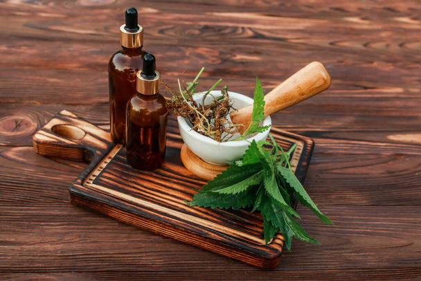 Fresh common nettle, stinging nettle or nettle leaf, or just a nettle root in ceramic mortar and pharmacy bottle with pipette. Ingredients for production of alternative medicine and homeopathic pills - Foto, imagen