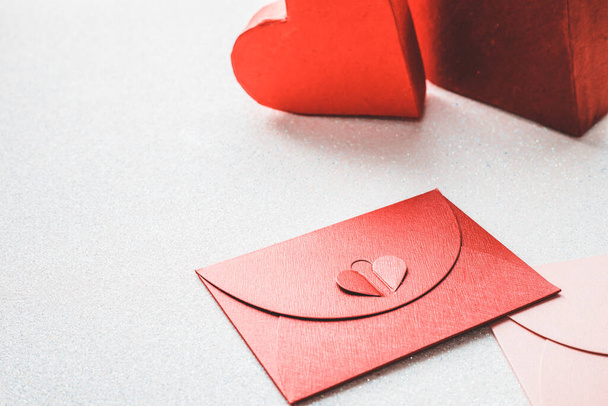 περιστασιακοί διακοσμητικοί κόκκινοι και ροζ φάκελοι με κλείσιμο που συμβολίζει την αγάπη σε ένα ασημί λαμπερό φόντο, κόκκινο φυσικό κουτί δώρου σε σχήμα καρδιάς για ένα αγαπημένο πρόσωπο Ένα μέρος για ευχές ή μια εξομολόγηση αγάπης  - Φωτογραφία, εικόνα