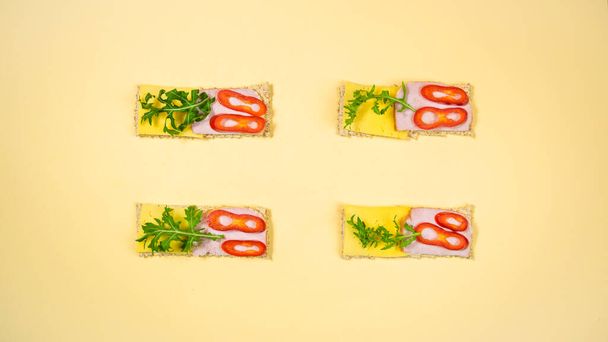 Four rectangular sandwiches with cheese, ham, arugula sprigs and slices of red pepper on whole grain crispbread. A healthy, nutritious yeast-free snack. Healthy nutrition concept. Flat lay. - Foto, Bild