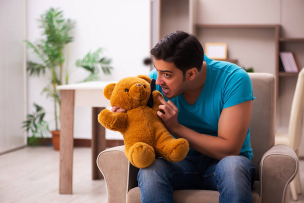 Jeune homme assis avec jouet ours à la maison - Photo, image
